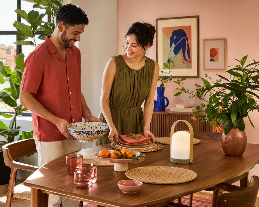 A couple styling a colorful dining table with ceramics and a portable lamp